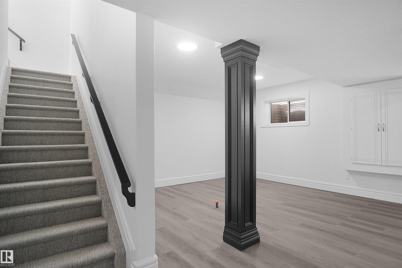 Staircase with carpeted treads and black handrail, recessed lighting, wood-finish flooring, built-in cabinetry, and a window with blinds - 6823 18 Avenue Sw, Edmonton, AB - Indoor Photo Showing Other Room