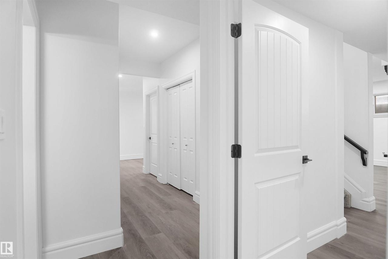 Hallway featuring wood-finish flooring, recessed lighting, white doors, and a black handrail - 6823 18 Avenue Sw, Edmonton, AB - Indoor Photo Showing Other Room