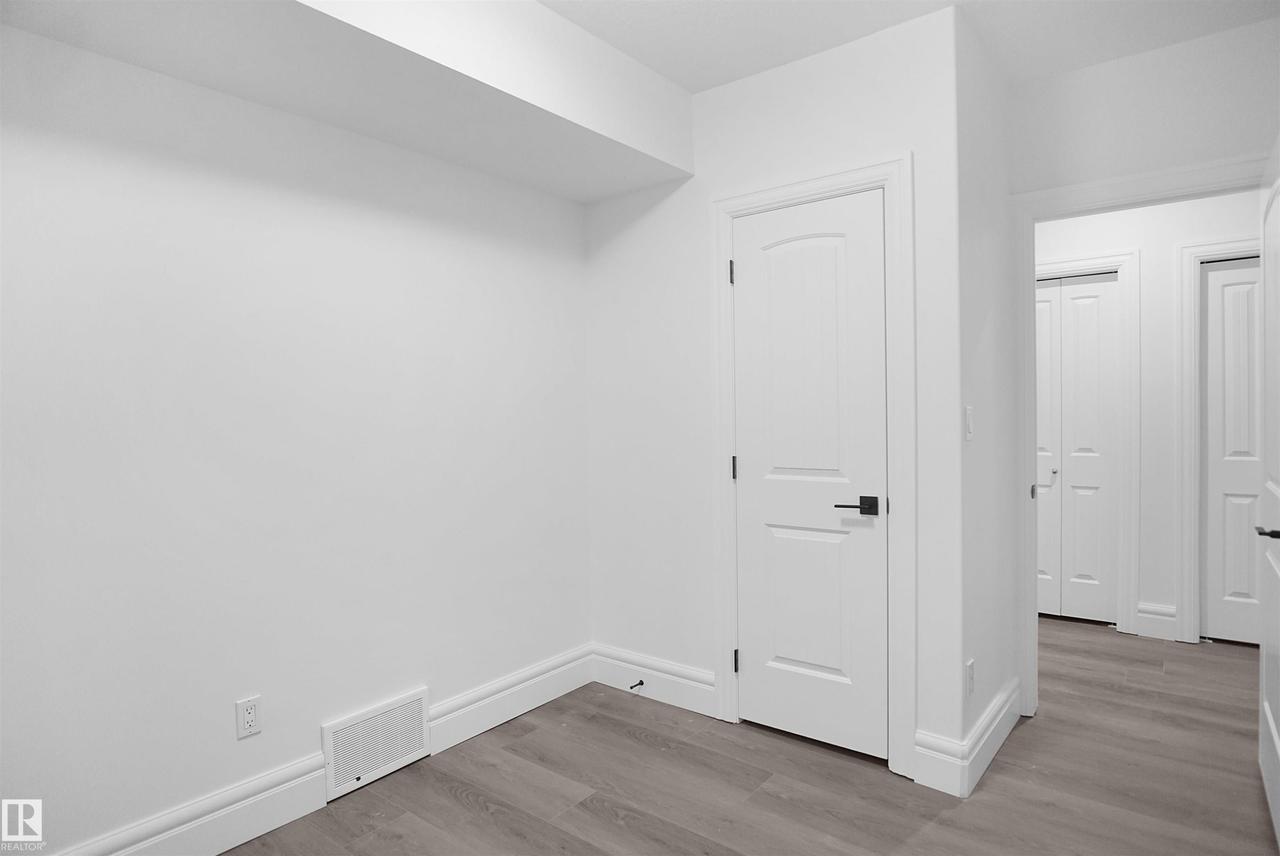 Freshly painted walls, wood-finish flooring, and white trim - 6823 18 Avenue Sw, Edmonton, AB - Indoor Photo Showing Other Room