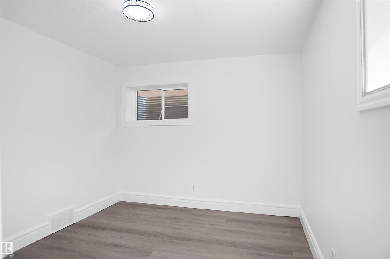 White painted walls with wood-finish flooring, featuring a flush-mount ceiling light and a single window - 6823 18 Avenue Sw, Edmonton, AB - Indoor Photo Showing Other Room